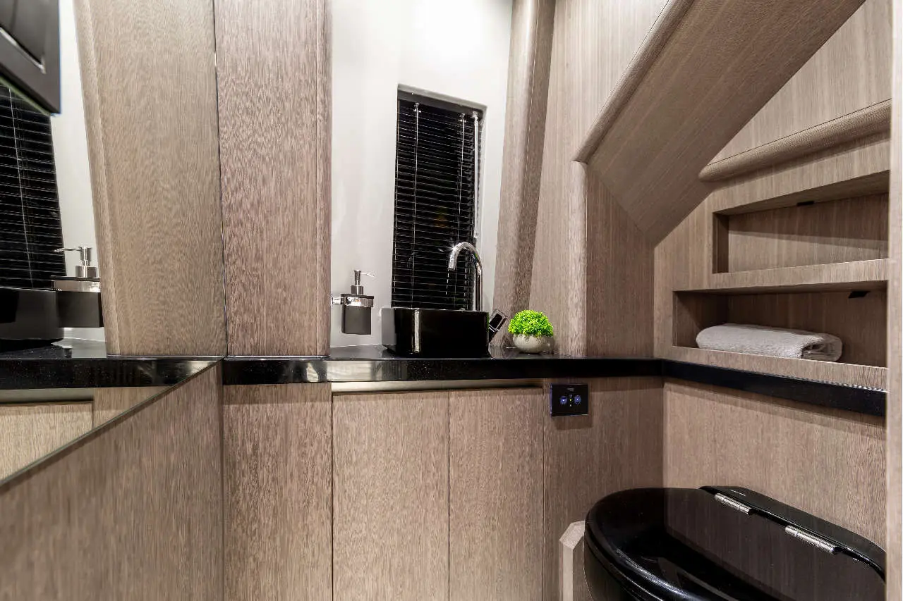 Modern bathroom featuring wooden panels, black sink, towel, and decorative plant, with a washbasin faucet and ambient lighting.