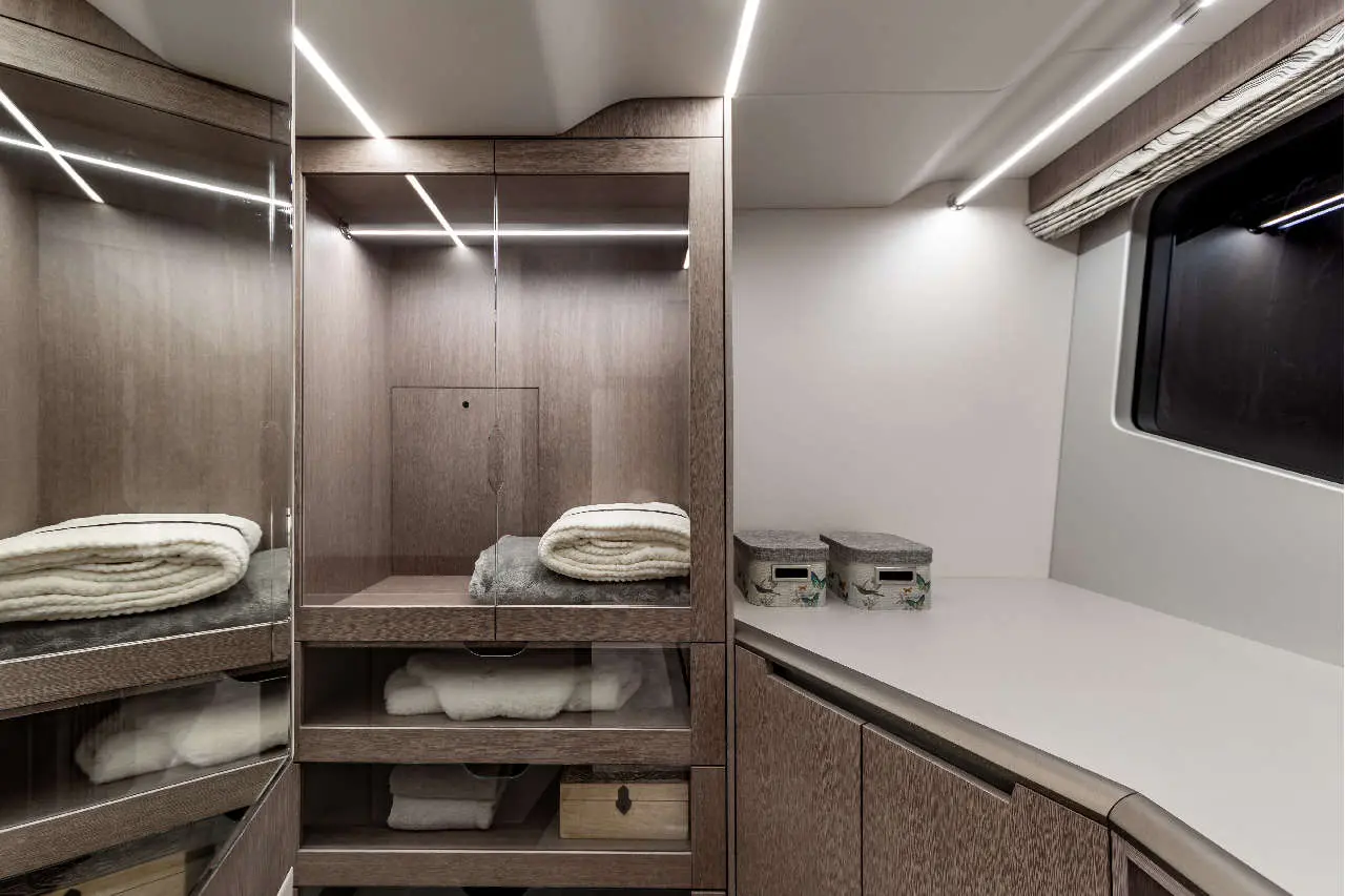 Sleek modern interior featuring wooden cabinets, mirrors, stacked towels, and decorative storage boxes against a bright backdrop.
