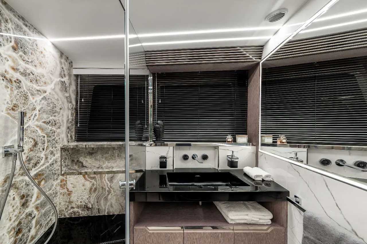 Modern bathroom featuring marble walls, a black sink, towels, and decorative items, with a well-lit, sleek design.