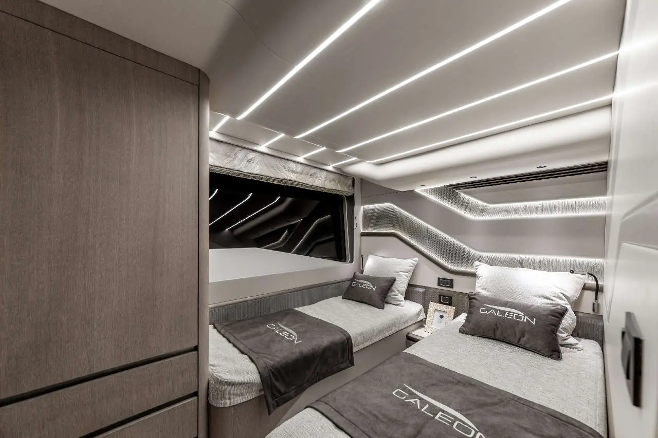 Modern yacht cabin interior featuring two single beds with grey linens, pillows, and 