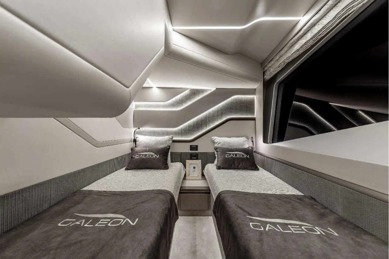 Interior of a modern yacht cabin featuring two single beds with 'GALEON' branded pillows and stylish contemporary design.