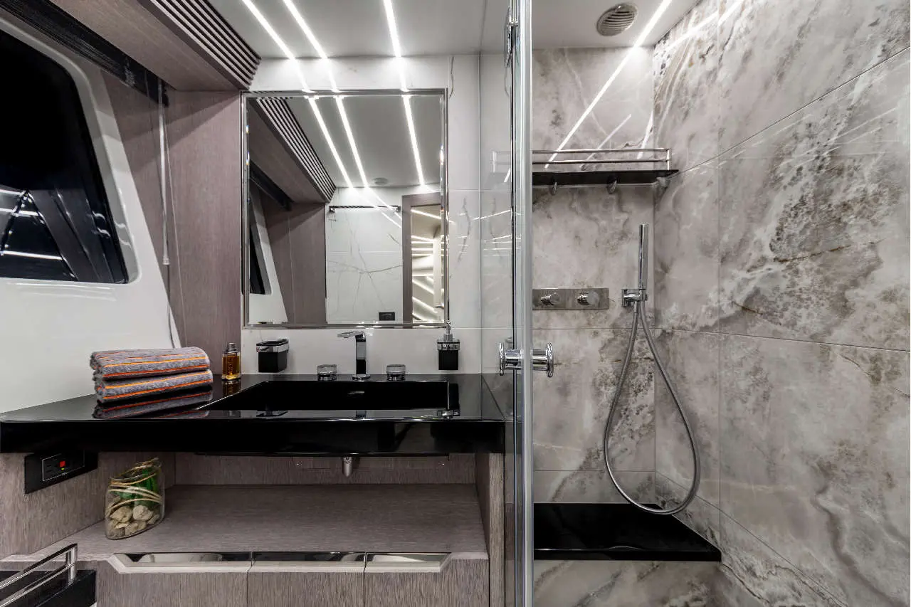 Modern bathroom with marble walls, a black sink, shower, mirror, and neatly arranged towels on a shelf.