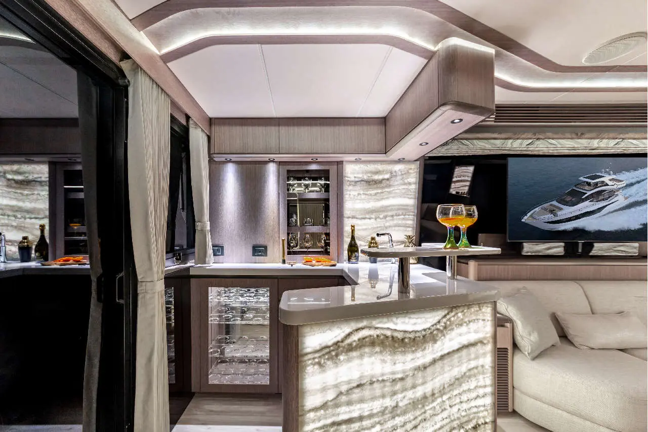 Luxurious yacht interior featuring a stylish bar, illuminated cabinetry, and a TV displaying a motor yacht on water.