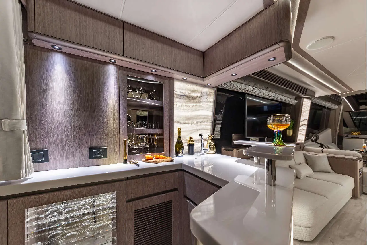 Modern yacht interior featuring a sleek bar with champagne, orange slices, and a cocktail glass, elegantly lit with soft lighting.