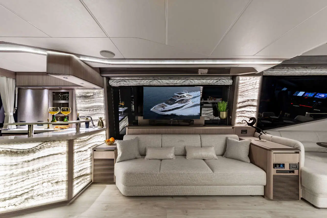 Luxurious yacht interior featuring a plush sofa, illuminated bar with cocktails, and a TV displaying a yacht on water.