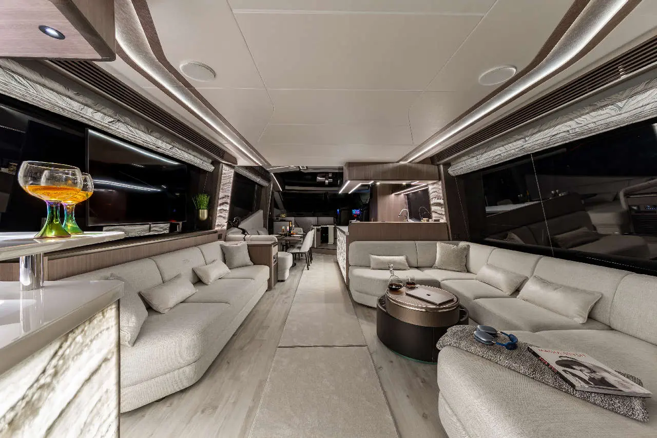 Luxurious interior of a yacht featuring a stylish lounge with sofas, coffee table, and ambient lighting. Glass with drink visible.