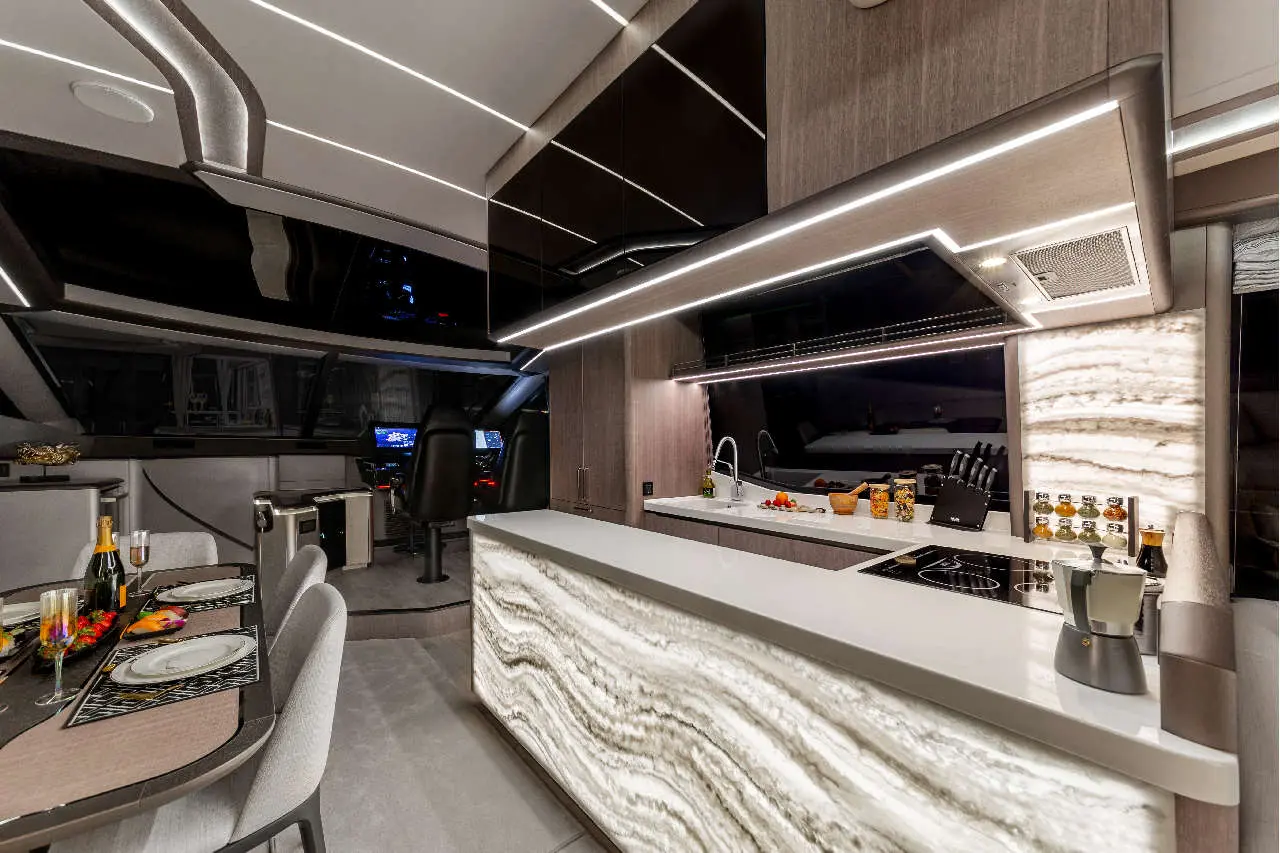 Modern yacht interior featuring a sleek kitchen, dining table with food, and a captain's helm visible in the background.