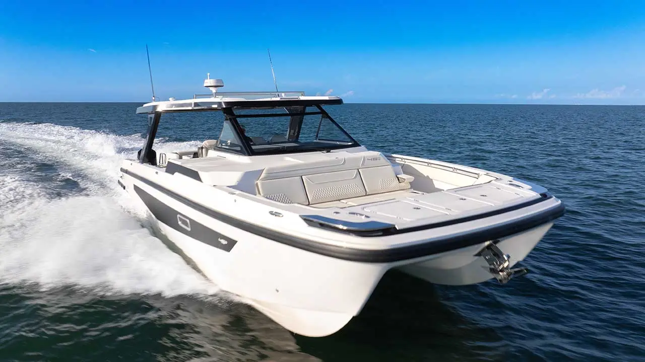 White luxury motorboat speeding across the open sea, creating a foamy wake beneath a clear blue sky.