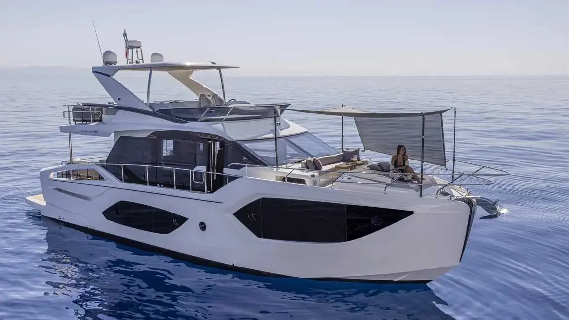 Luxury motor yacht cruising on calm blue sea, with a woman seated beneath the foredeck sunshade.