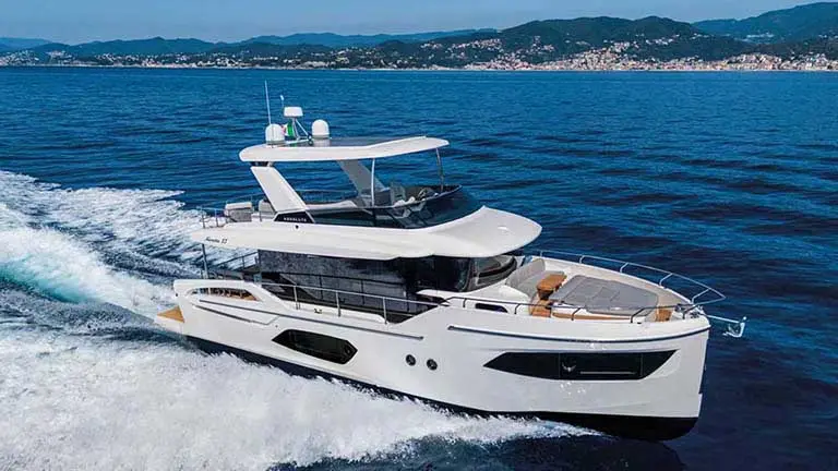 White luxury motor yacht cruising on blue sea, leaving a wake, with mountainous coastline in the background
