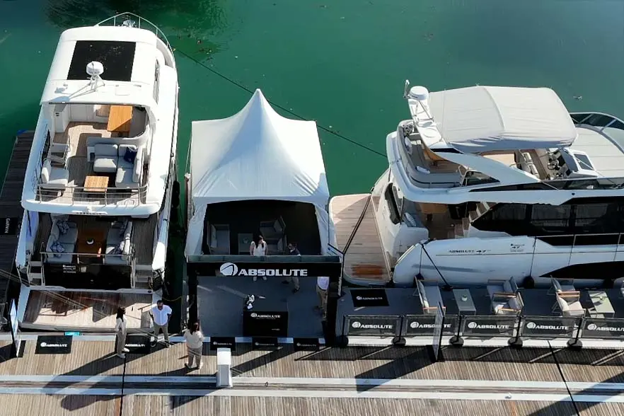 Two luxury yachts docked beside a promotional tent displaying 