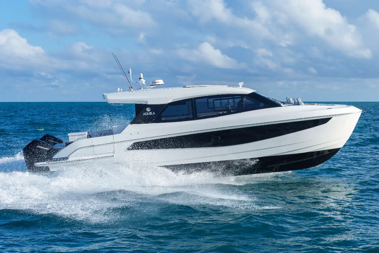 Aquila powerboat cruising on water, creating splashes, with a clear sky and clouds in the background.