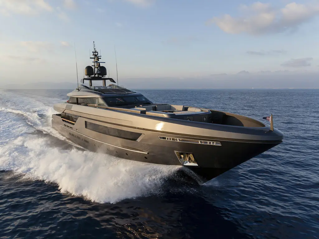 A sleek luxury yacht speeds through clear waters, creating white foam trails under a bright, cloudy sky.