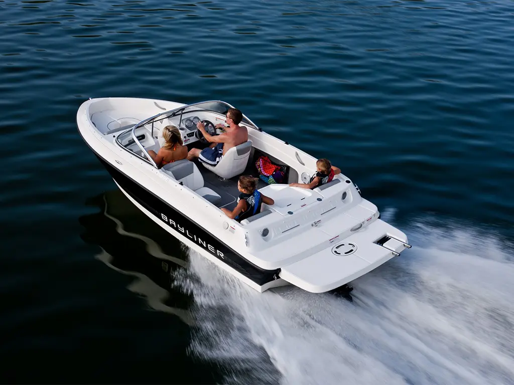 A Bayliner boat speeds across calm water with two adults and two children enjoying a sunny day on the lake.