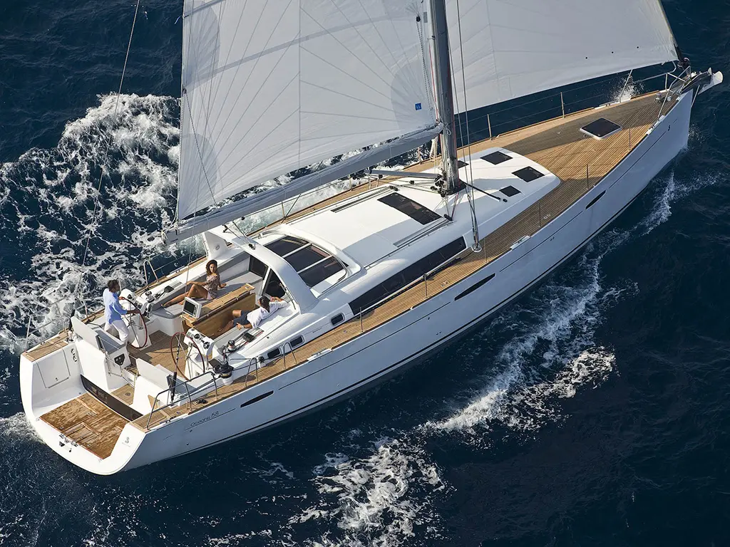 Sailing yacht with three people on deck navigating through deep blue waters, with sunlight reflecting off the waves.