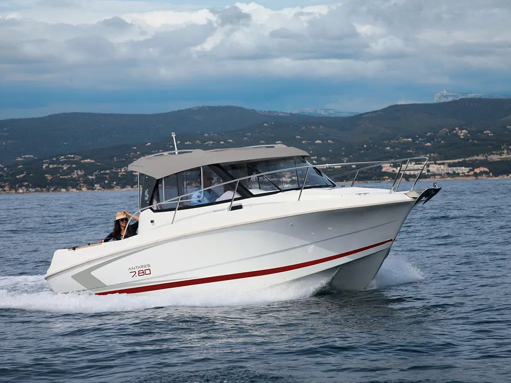 A white motorboat named Antares 7.80 speeds through calm waters, with mountains and cloudy sky in the background.