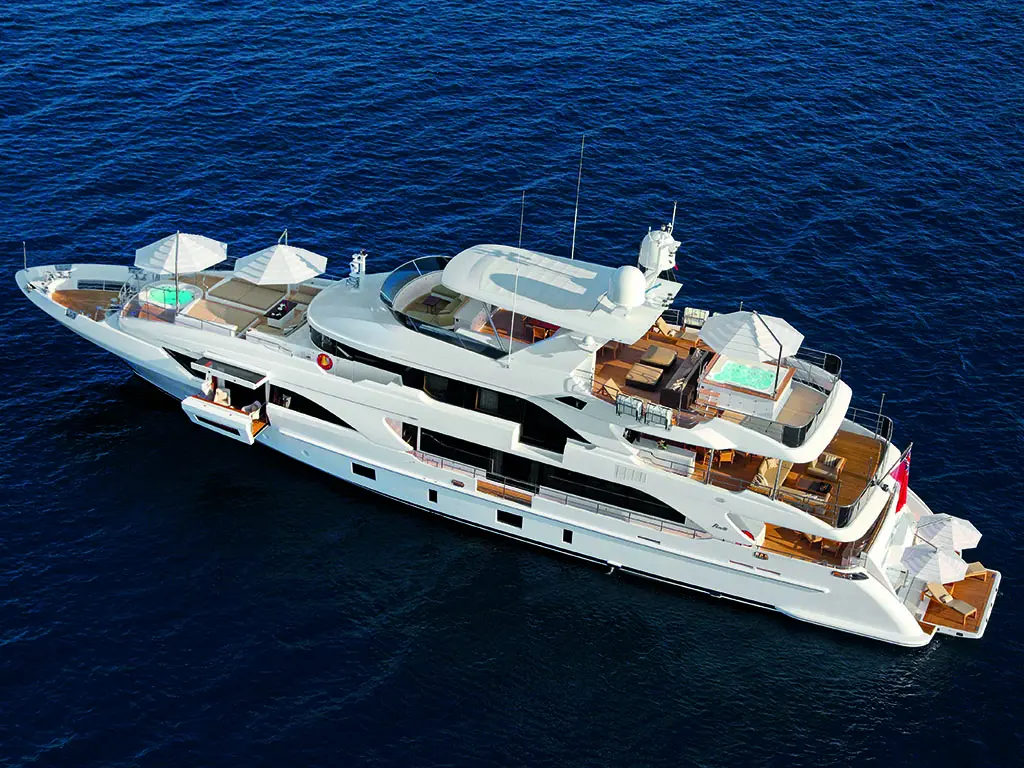 Luxury yacht floats on blue water, featuring shaded lounging areas and a small pool on the upper deck with umbrellas.