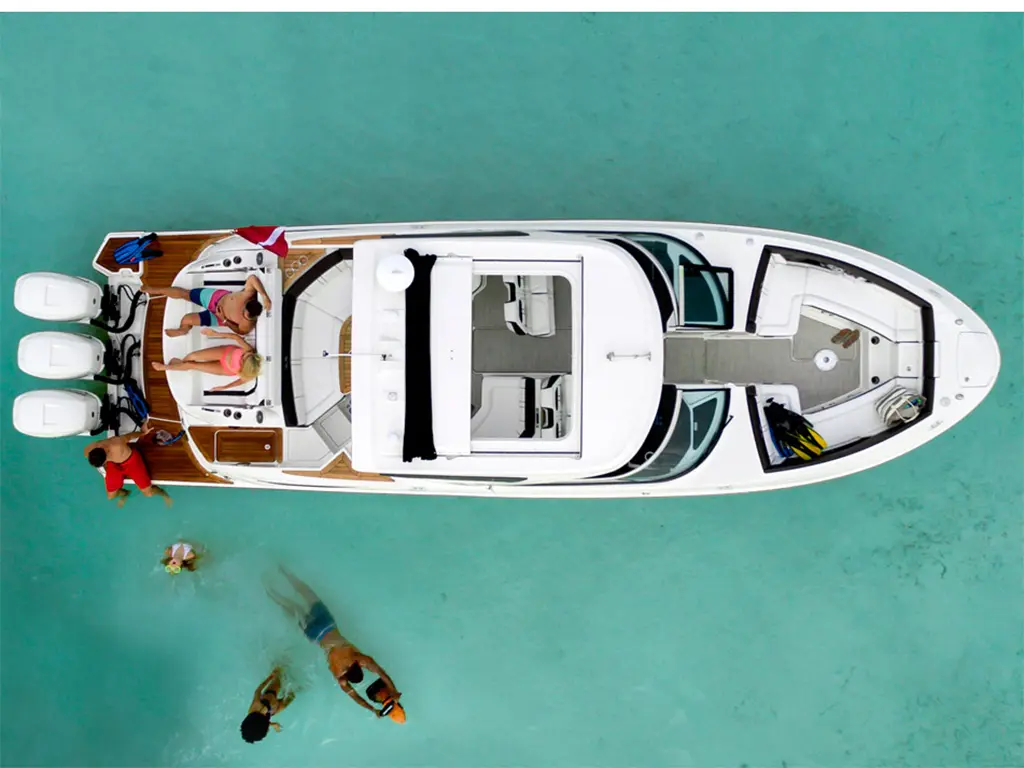 Aerial view of a sleek boat with people relaxing, swimming, and enjoying water activities in clear turquoise waters.