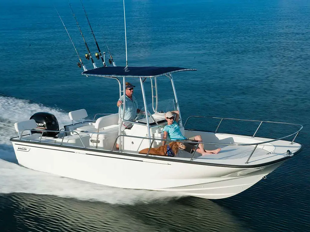 A man steers a white boat with fishing rods, while a woman relaxes with a dog on the deck in calm blue waters.