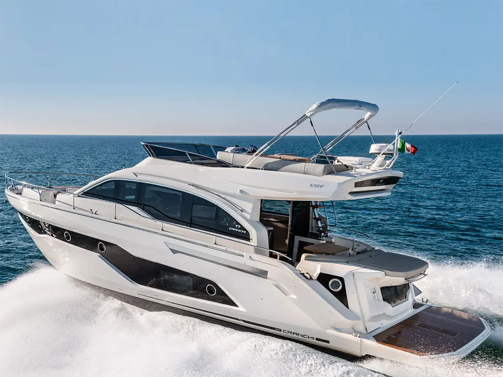 A sleek white motor yacht navigates through the blue waters, showcasing a stylish design and Italian flag on display.