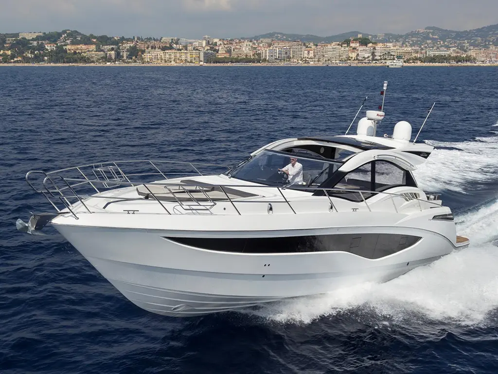 A sleek white yacht sails through blue waters, with a driver at the helm and a scenic coastline in the background.