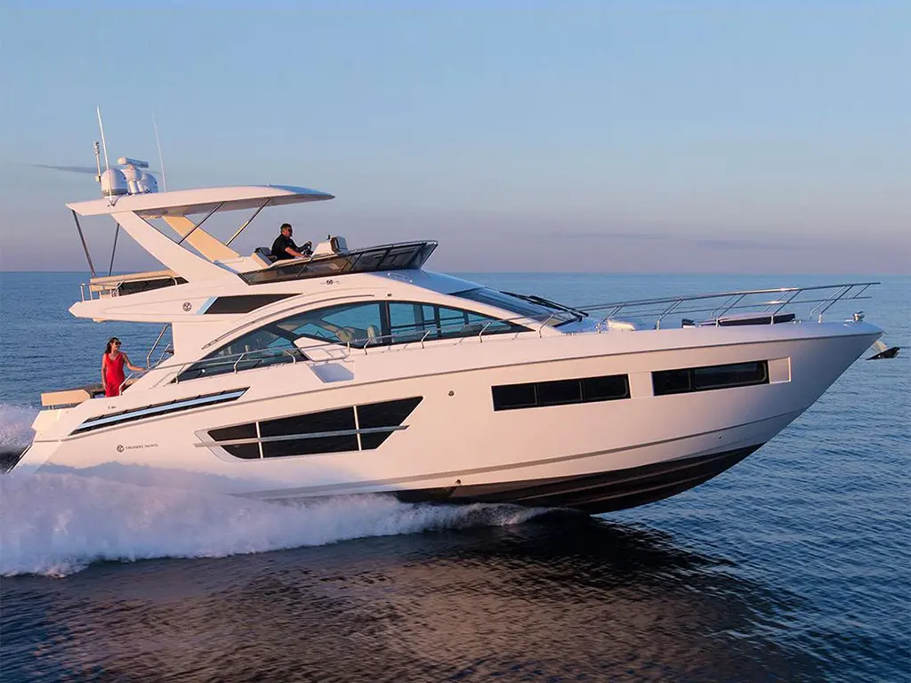 Luxury motor yacht cruising on calm waters, with a man at the helm and a woman enjoying the view in a red dress.