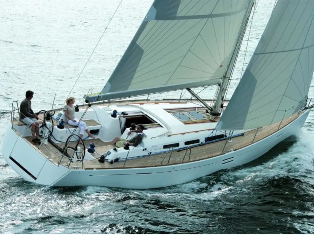 A modern sailing yacht gliding across water with three people on board, enjoying a sunny day at sea.