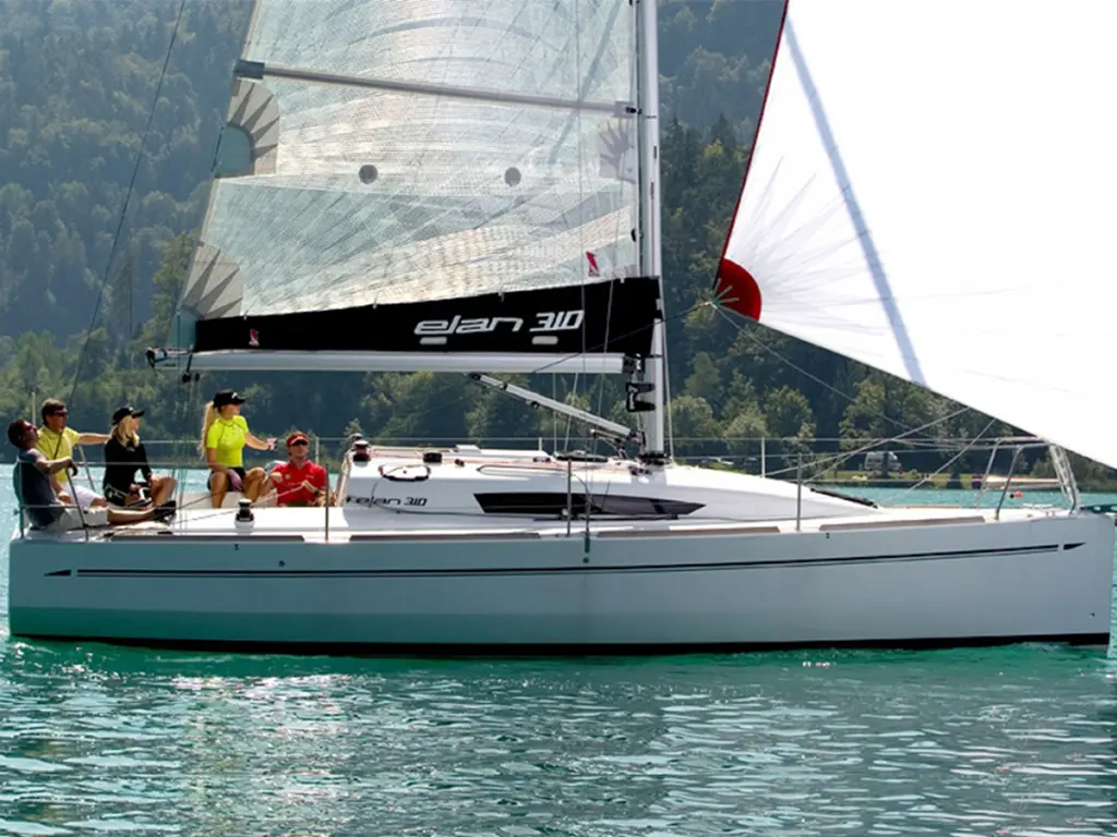 A group of five people enjoying sailing on an Elan 310 yacht, surrounded by turquoise waters and mountains in the background.