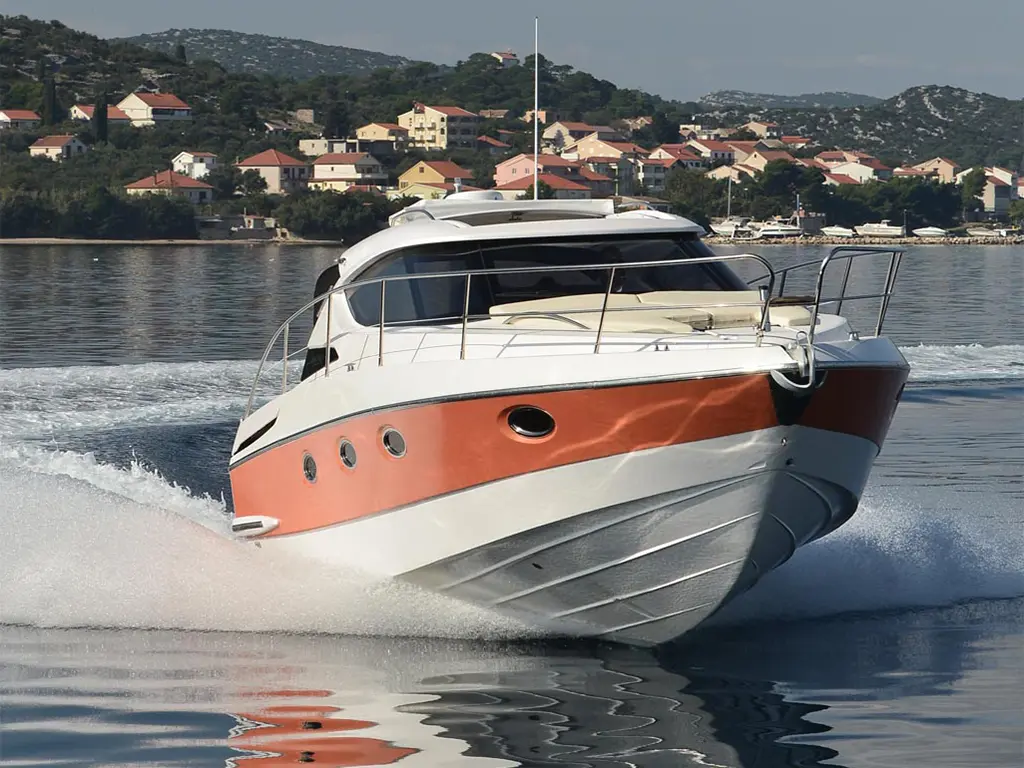 A luxury motorboat speeds through calm waters with a picturesque coastal village in the background.
