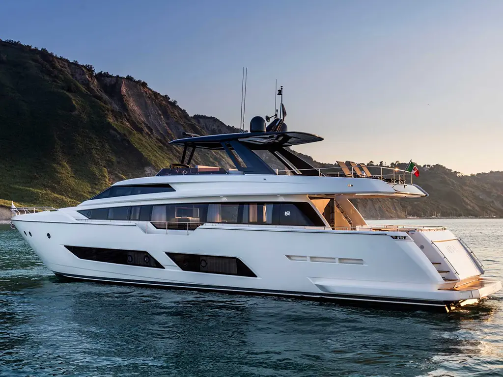 Luxury white yacht anchored near a green hillside, with blue water and a clear sky, featuring modern design elements.