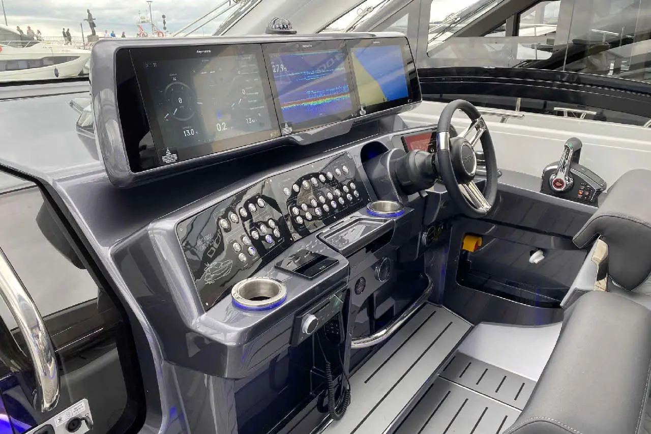 Modern boat cockpit showcasing sleek dashboard with digital screens, numerous controls, and a steering wheel.