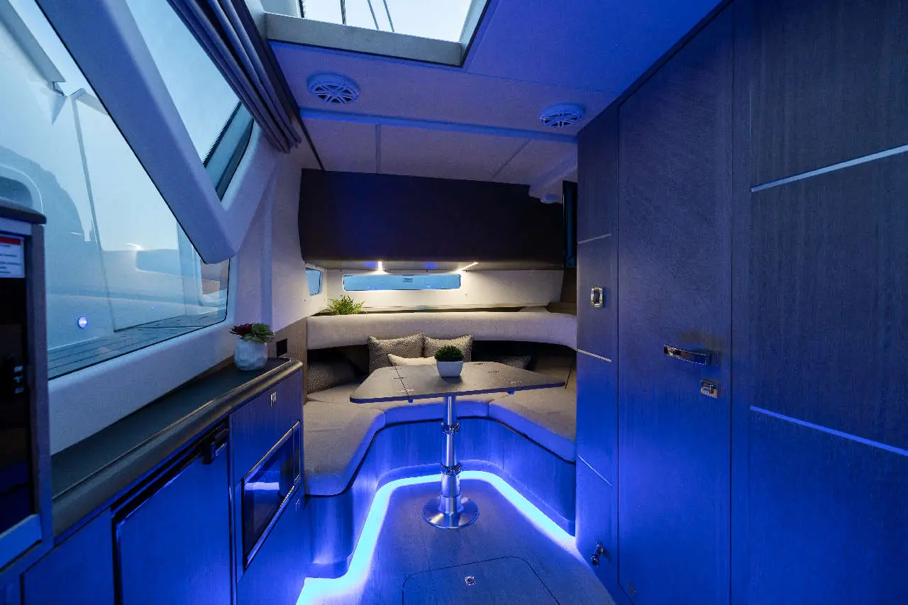 A modern boat interior featuring a lounge area with grey cushions, a table, and blue ambient lighting under the seating.