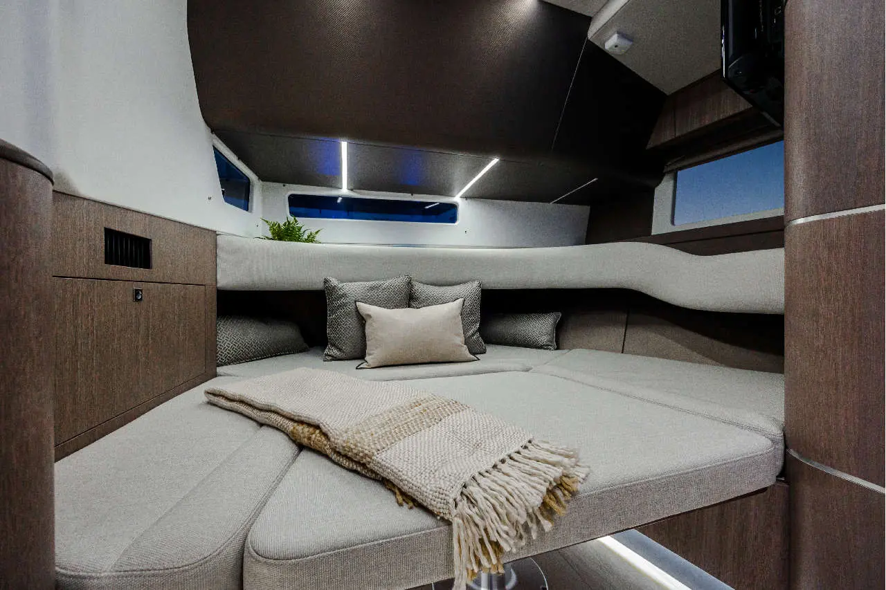 Modern boat interior featuring a grey seating area with cushions, a woven throw, and a decorative plant near large windows.