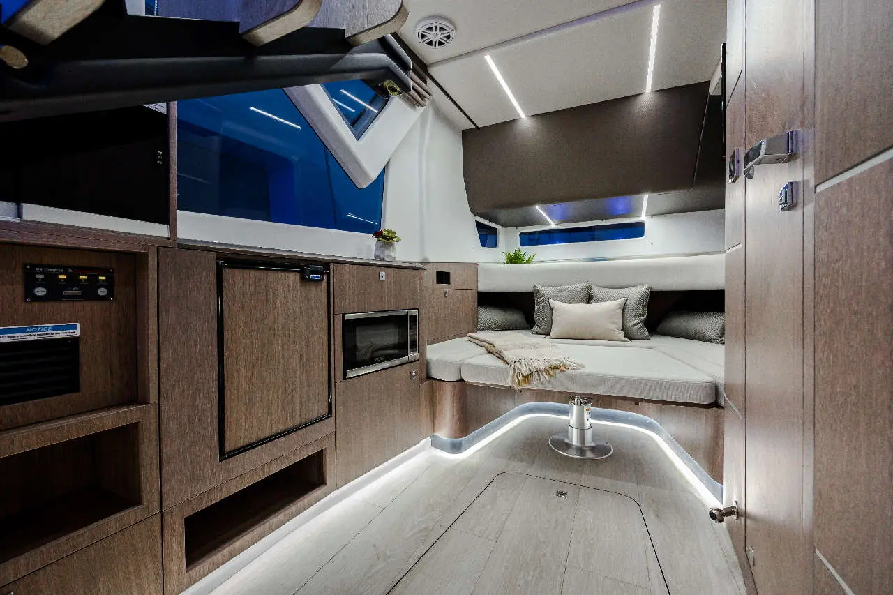 Modern boat interior featuring a lounge area, kitchen appliances, soft furnishings, and ambient lighting.