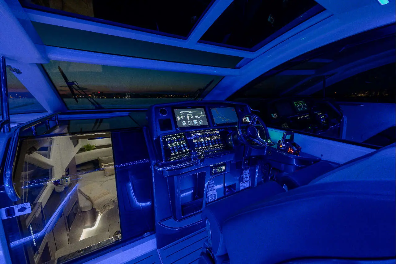 Luxury yacht cockpit with blue ambient lighting, featuring advanced navigation screens and a sleek steering wheel.
