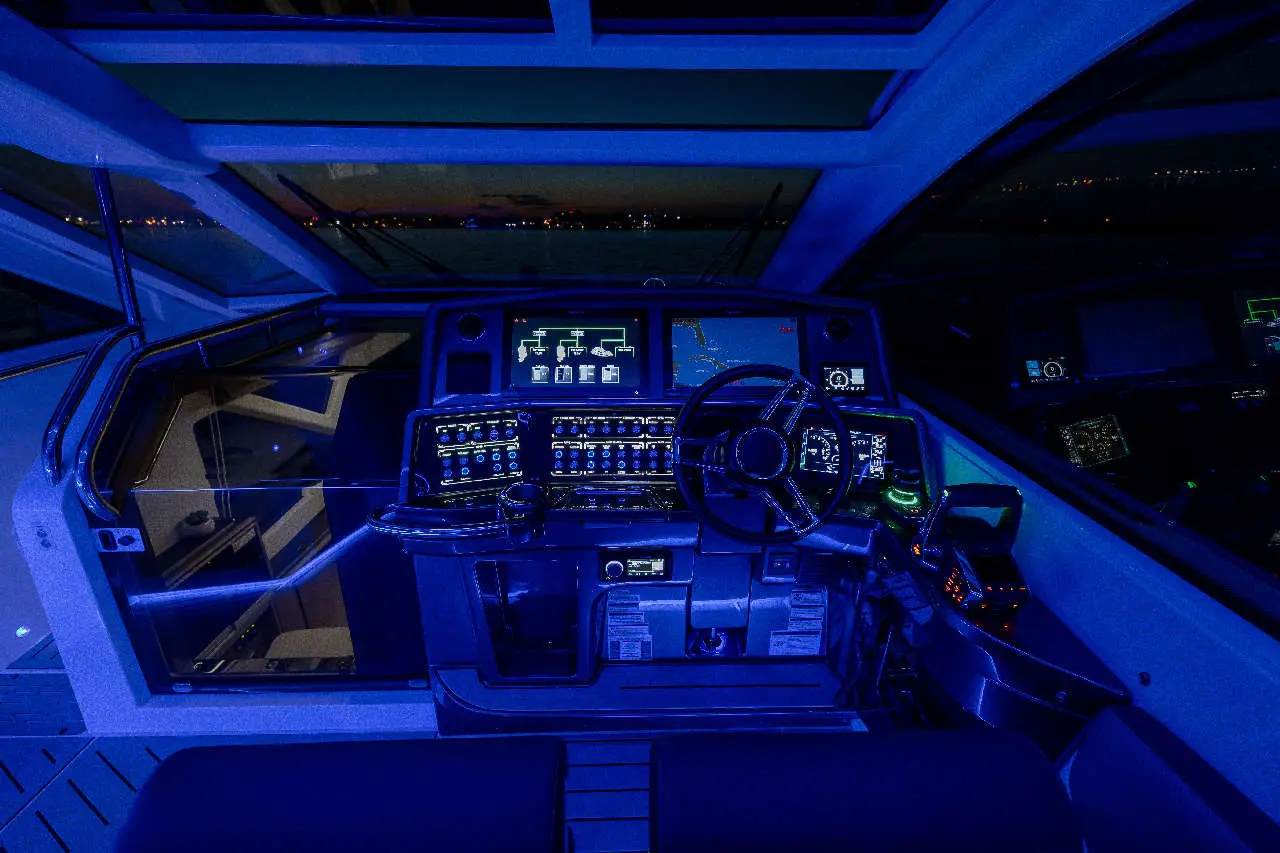 Luxury boat cockpit with illuminated controls, navigation screens, and a panoramic view of the night water.