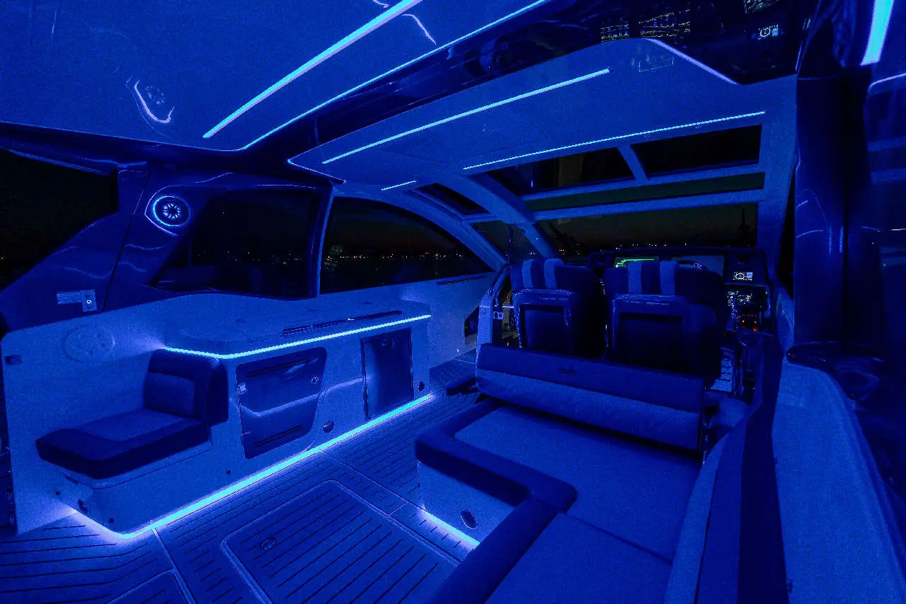 Luxurious boat interior illuminated with blue LED lights, featuring stylish seating and modern controls against a night backdrop.
