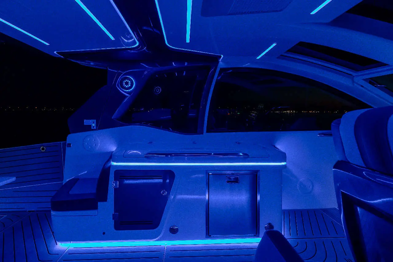 Interior of a luxury boat with blue LED lighting, featuring a sleek design and modern amenities, viewed at night.