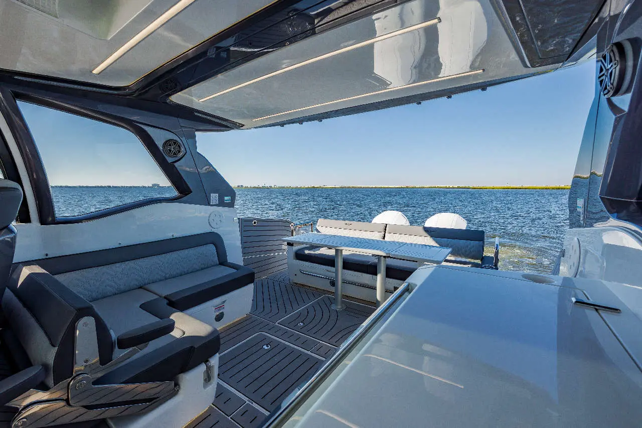 Interior view of a modern boat, featuring cushioned seating, a dining table, and a scenic backdrop of the water and sky.
