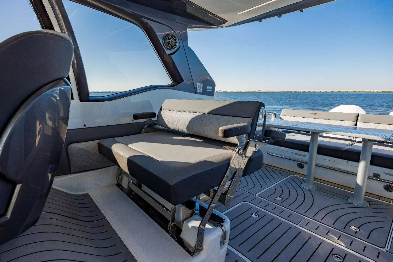 Interior view of a boat showing a grey folding seat, flat surface, and scenic water background under clear blue skies.