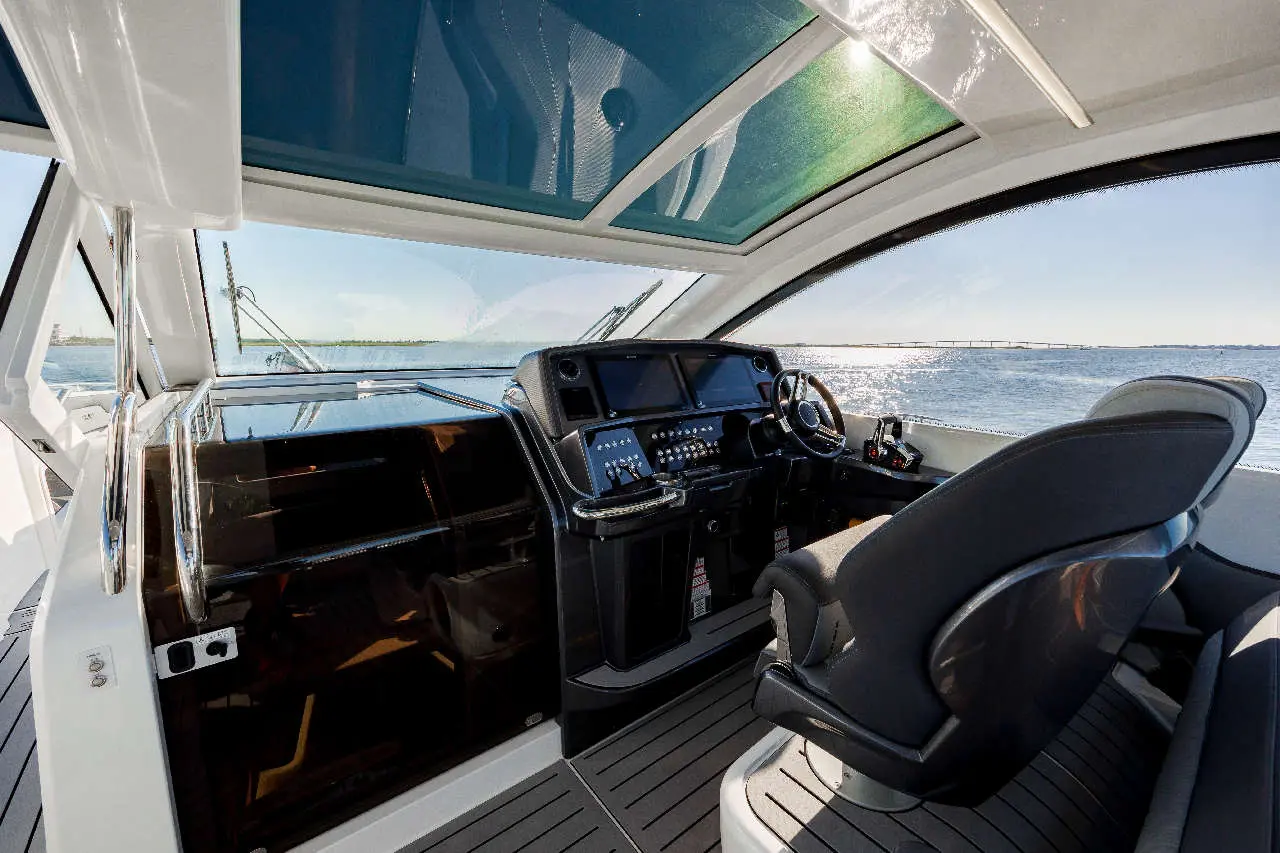 Luxury yacht interior featuring a steering wheel, control panel, and panoramic windows overlooking the water.