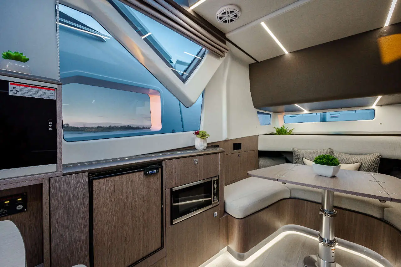 Modern boat interior featuring a compact kitchenette, dining area, large windows, and contemporary lighting.