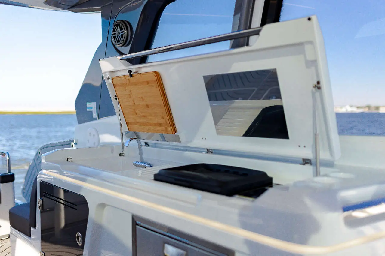 A modern boat's galley featuring a wooden cutting board, sink, and scenic water view through a large window.