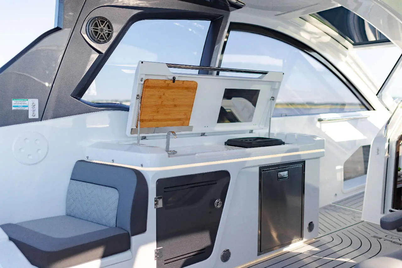 Modern boat interior featuring a cooking area with a wooden cutting board, storage, and a grey upholstered seat.