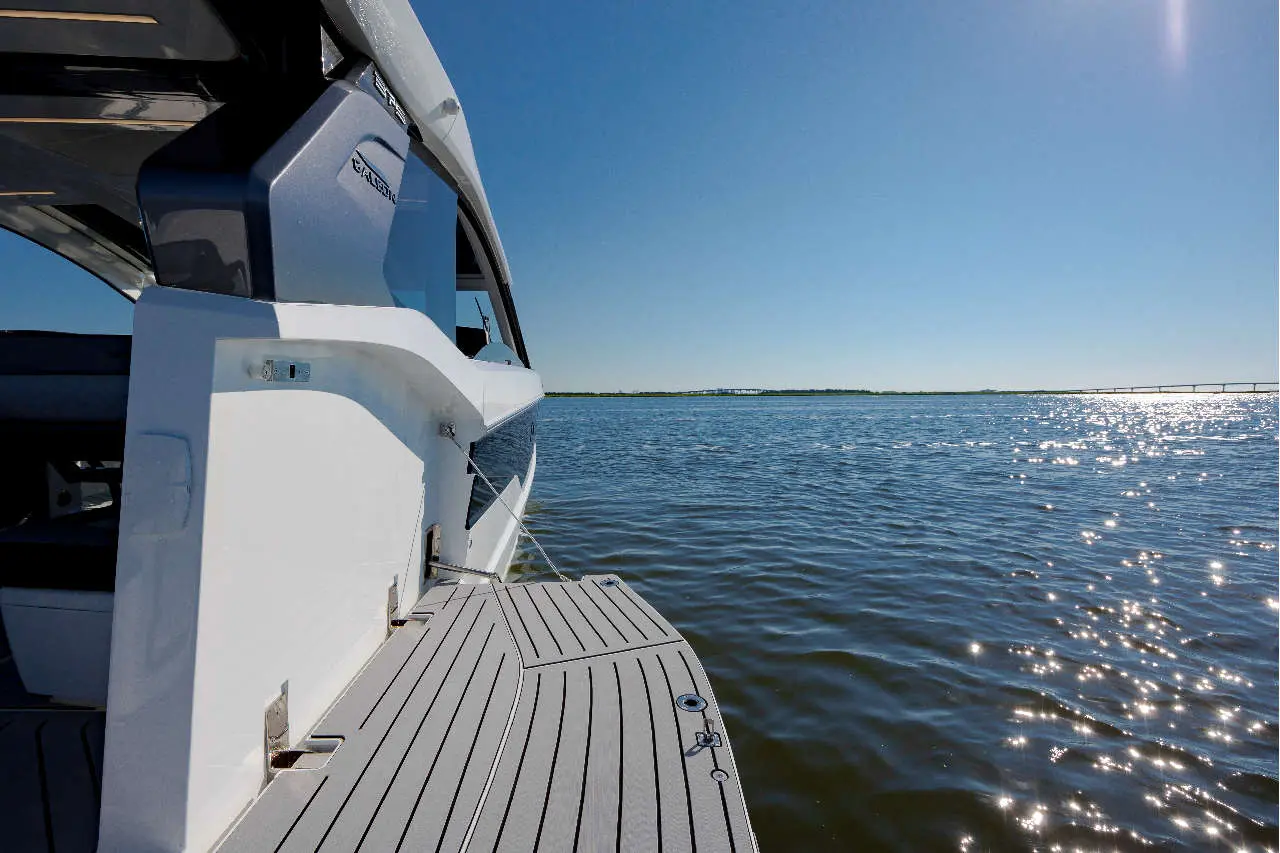 A luxury yacht's side view on calm water, with sunlight reflecting off the surface and a distant bridge visible.