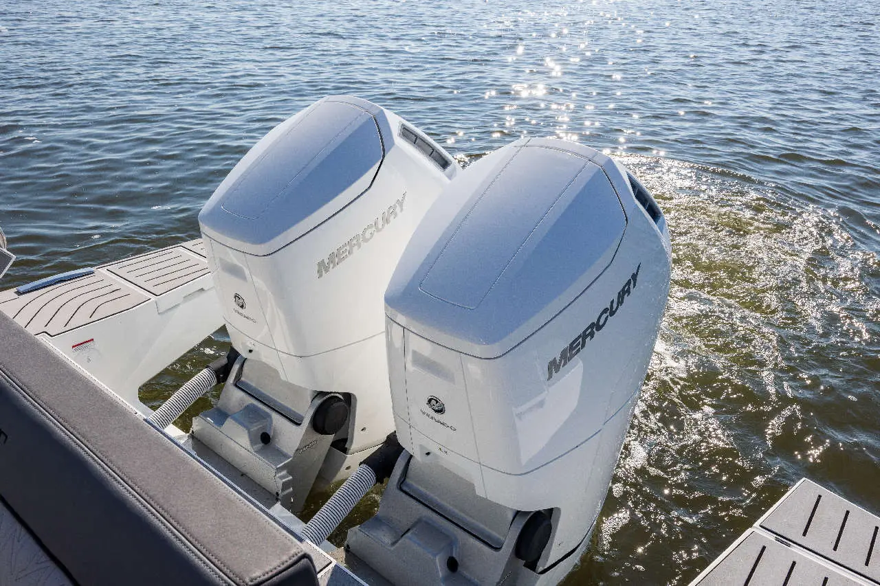 Two Mercury outboard motors mounted on a boat, with rippling water and sunlight reflecting on the surface.