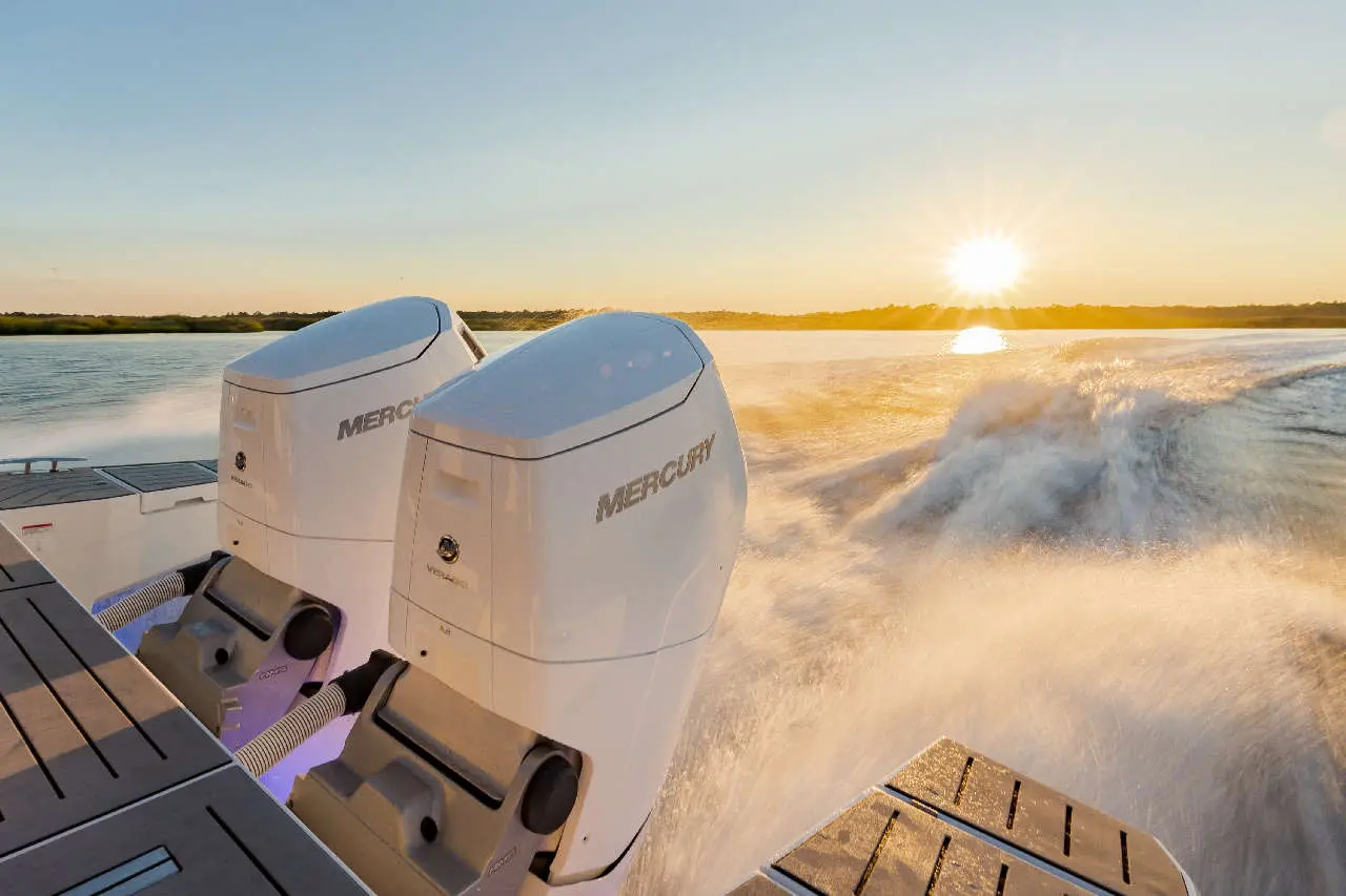 Two Mercury outboard motors on a boat, producing spray as the sun sets over a calm waterway.