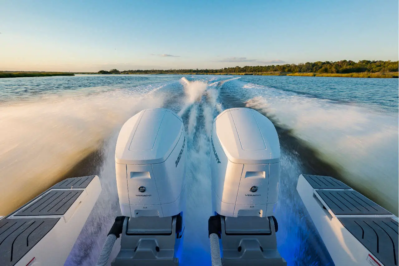 Twin Mercury Verado outboard motors powering a boat, leaving a wake on a calm river under a clear sky.