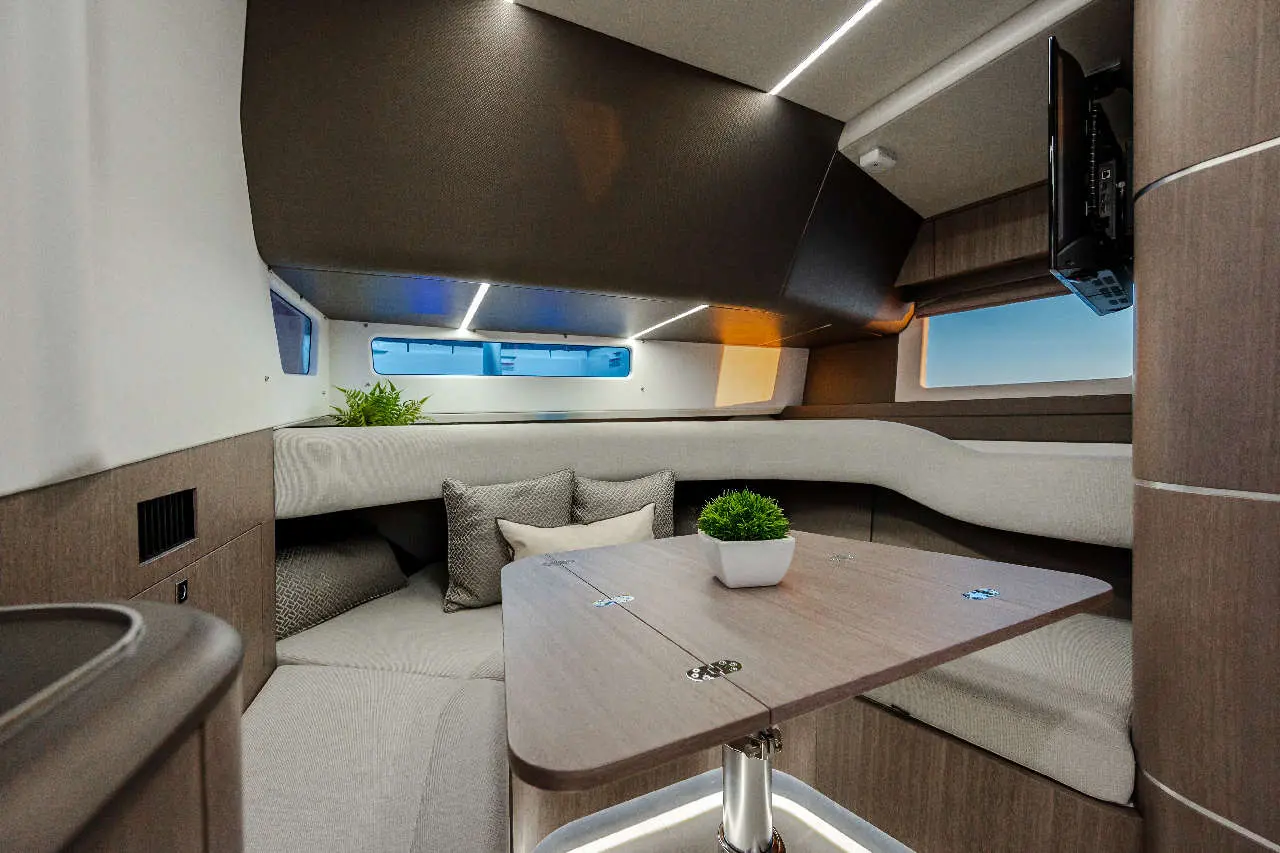 Modern boat interior featuring a sleek table, plush seating, and large windows with a potted plant enhancing the space.