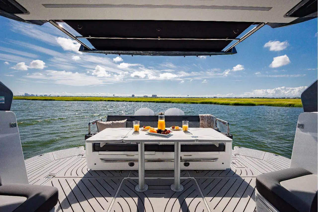 A scenic view from a boat, featuring a dining table with drinks and food, surrounded by water and green wetlands under a blue sky.